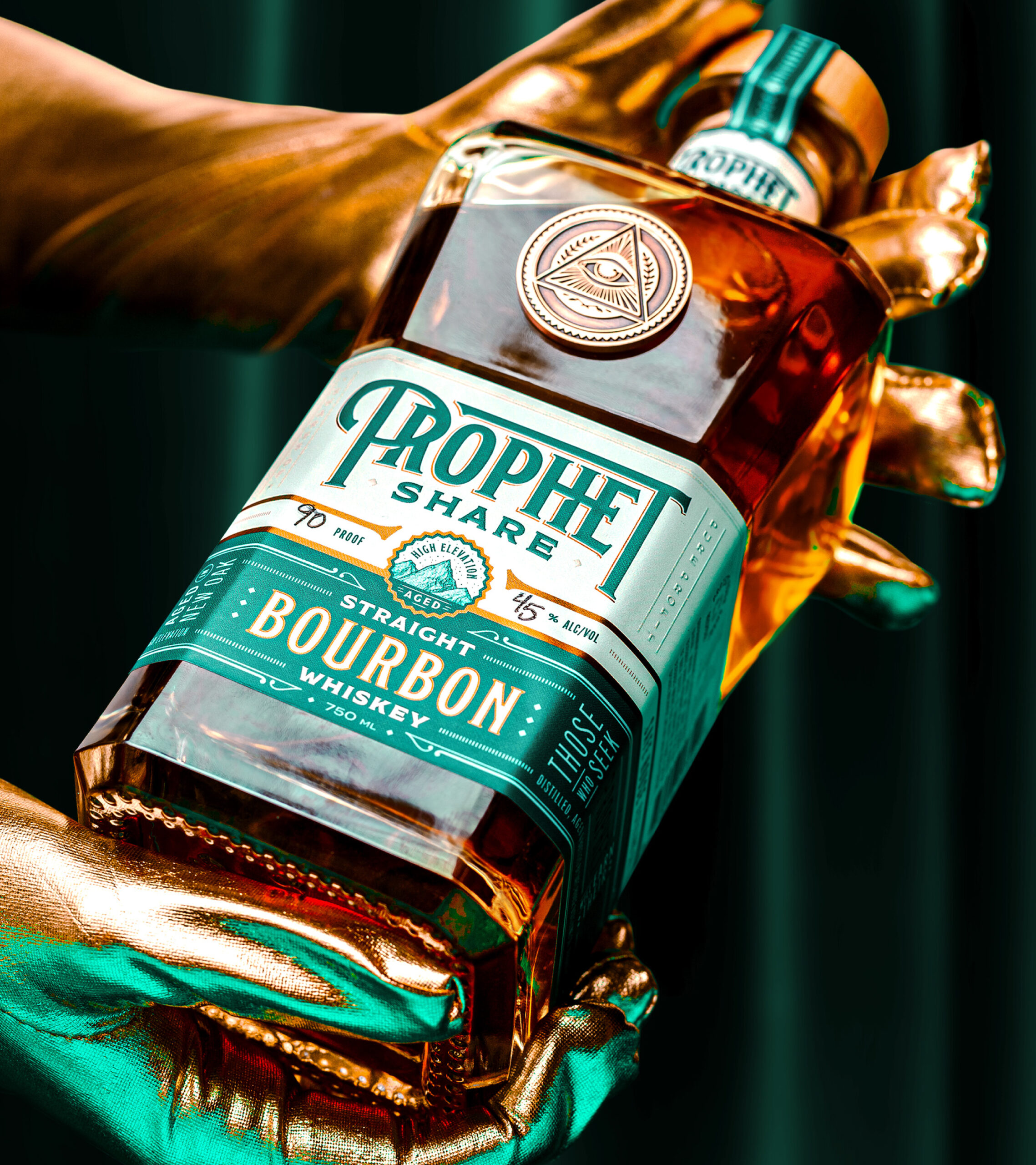 Prophet Share bottle being held by a pair of hands with golden gloves against a green velvet curtain in the background