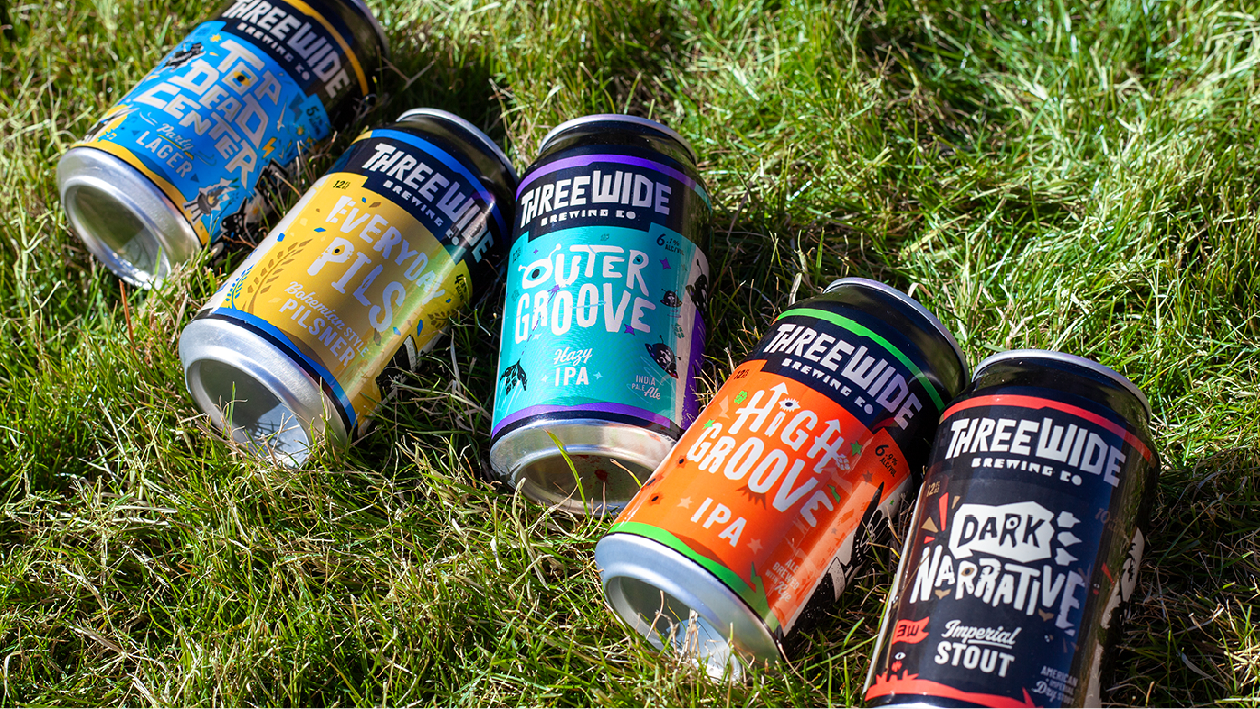 Photo of the 5 signature Three Wide beers in a lineup laid on the grass naturally. 