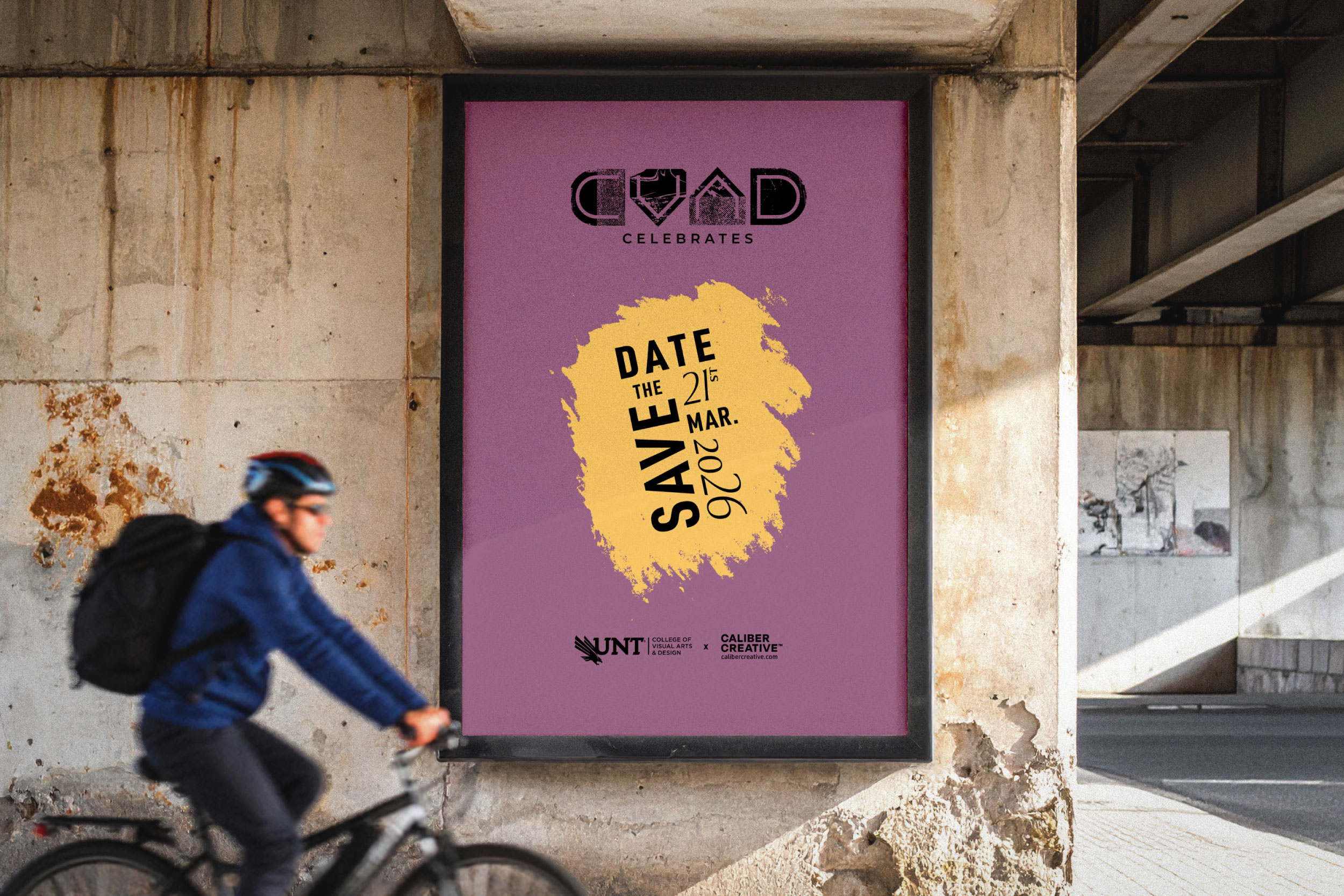 Image of a cycler passing by a billboard with CVAD Celebrates branding and Save the Date information displayed. 